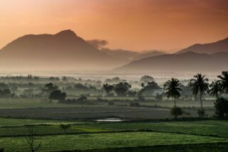 Indian nature beautifully represented in the colors of its national flag: lush green fields symbolizing growth, golden-orange hues of the sunset reflecting courage, and soft white smoke drifting gracefully through the scene, embodying peace and harmony.